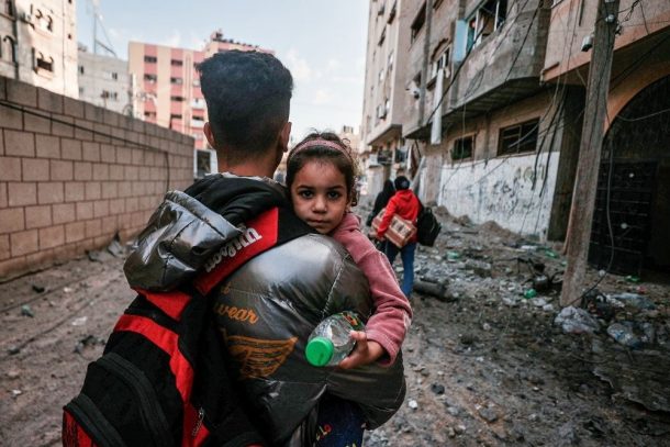 Far bærer sit barn på armen mellem ruiner i Gaza