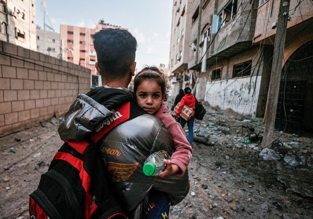 Far bærer sit barn på armen mellem ruiner i Gaza