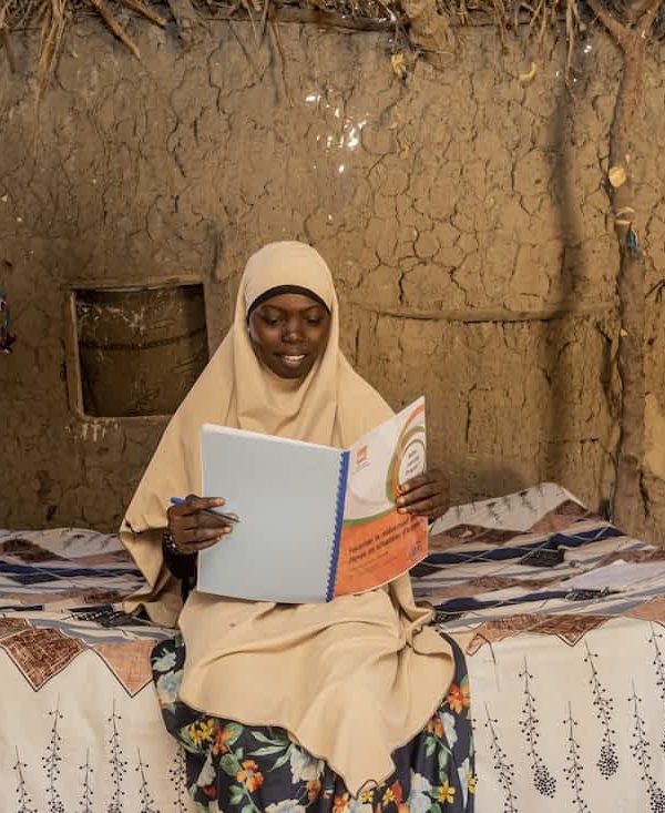 Zahara Seybou Harouna, Niger, sidder på sengen i sit hjem med en bog i hænderne og læser.