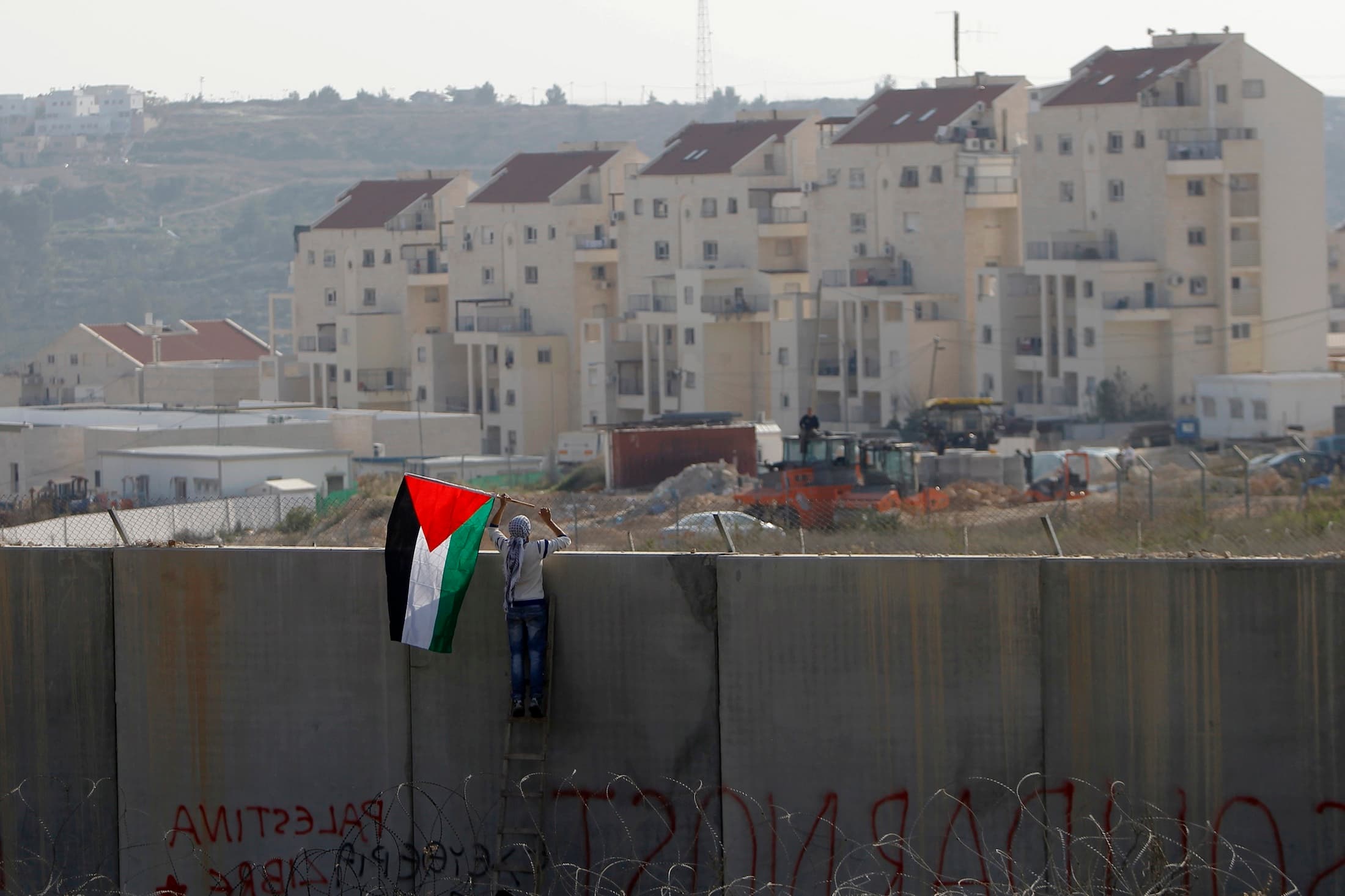 A Palestinian protester places a flag on the controversial Israeli barrier during clashes with Israeli security officers near Ramallah